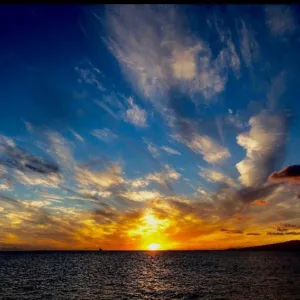 Sailboat gliding past Honolulu skyline at sunset