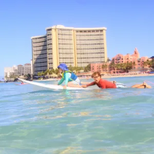Instructor guiding beginner on surfboard in calm water