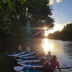 People practicing SUP yoga on calm water at sunset