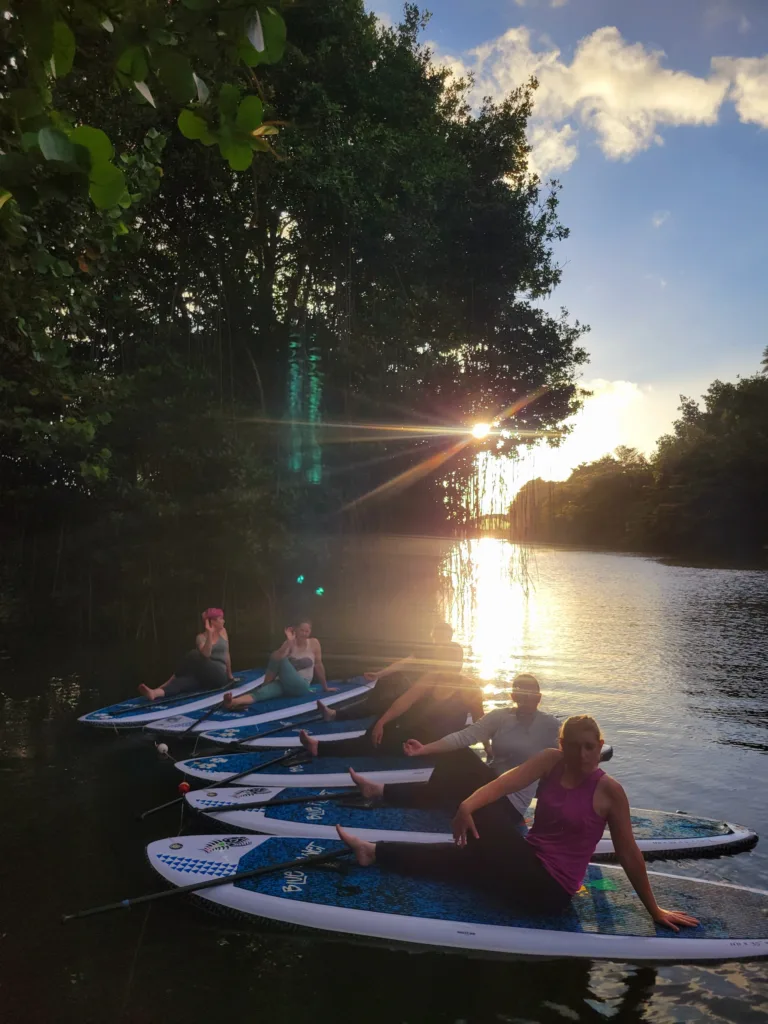 People practicing SUP yoga on calm water at sunset