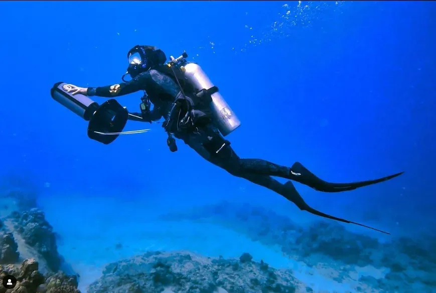 Scuba diver using propulsion vehicle under clear ocean water