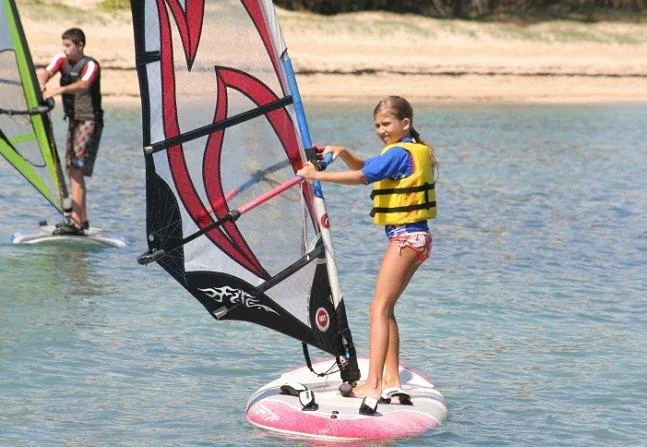 Children learning windsurfing on calm ocean waters