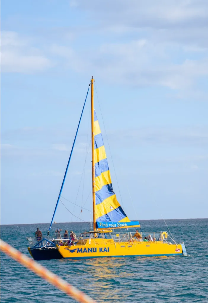 Sailboat gliding across calm waters at Manu Kai Harbor sunset