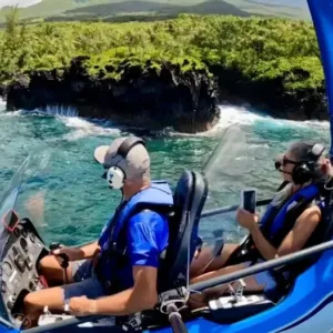 Pilot flying autogyro over Maui coastline with clear blue skies