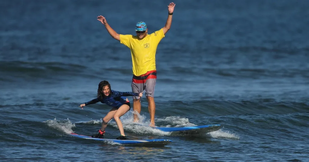 Instructor teaching individual how to surf on beach