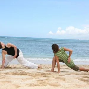Yoga class practicing on sandy beach under tree shade