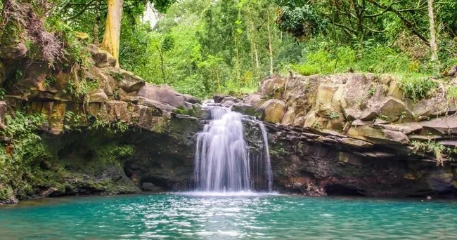 Hiker crossing a stream near a tropical waterfall