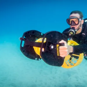Experienced diver riding underwater scooter near coral reef