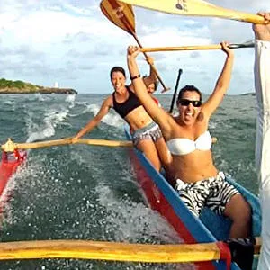 Group paddling traditional Hawaiian outrigger canoe on calm sea
