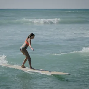 Instructor guiding a beginner on a surfboard in warm ocean waters