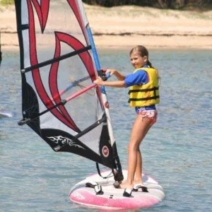 Children learning windsurfing on calm ocean waters